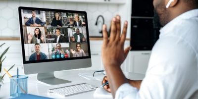 Video call, online conference. Over shoulder view of african american man at computer screen with multinational group of successful business people, virtual business meeting, work from home concept Video call, online conference. Over shoulder view of african american man at computer screen with multinational group of successful business people, virtual business meeting, work from home concept