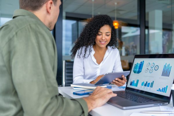 Business man and business woman in a meeting at the office. There is a laptop on the table showing finance charts and graphs