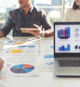 Group of people meeting with technology and paperwork. Group of people meeting with technology and paperwork. Close up of digital tablet and laptop computer with market analysis data on the screen. The documents have financial or marketing figures, graphs and charts on them. Multi ethnic group including Caucasian, latin and African American