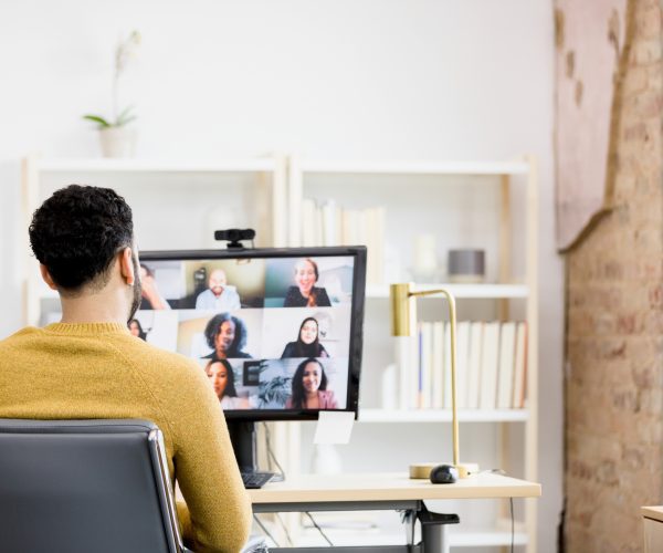 Over-the-shoulder view unrecognizable man using desktop PC for meeting An over-the-shoulder view of an unrecognizable man as he uses his desktop PC for a meeting with diverse co-workers.